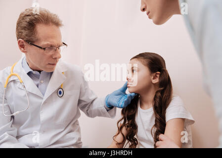 Wir werden es zu heilen. Zuständigen ausgebildeten lokalen Dermatologen mit speziellen Handschuhen und Blick auf seine kleinen Patienten Haut während sie sitzt in seinem Büro Stockfoto