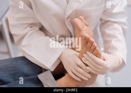 Sagen Sie mir, ob es Ihnen weh tut. Eingedenk dessen engagierte junge Spezialist mit professioneller Ausrüstung während der Prüfung mans Sohlen und Diagnose von ihm Stockfoto