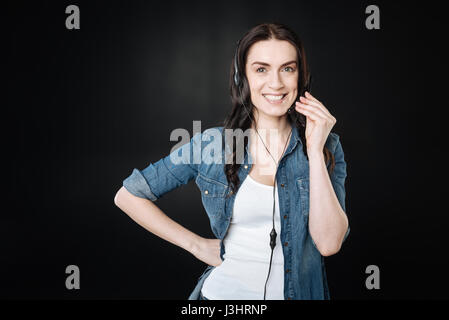 Casual-Style. Positiv begeistert Mädchen Lächeln auf ihrem Gesicht, Rechte Hand auf der Taille gedrückter Mikrofon in der linken Hand zu halten Stockfoto