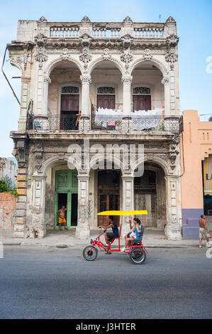 Havanna - Juni 2011: Fahrrad Taxi trägt einen Passagier vor bröckelnden Kolonialarchitektur in einer ruhigen Straße im Centro. Stockfoto