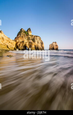 Wellen brechen sich am Strand von den drei Brüdern, mit Felsformationen im Hintergrund. Langzeitbelichtung Foto in Portimao, Algarve. Stockfoto
