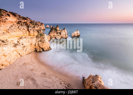 Wellen brechen sich am Strand von den drei Brüdern, mit Felsformationen im Hintergrund bei Sonnenuntergang. Langzeitbelichtung Foto. Stockfoto