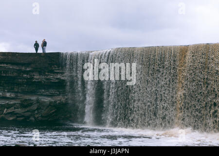 Menschen stehen auf Jagala Wasserfall, der höchste natürliche Wasserfall in Estland mit etwa 8 Meter Höhe. Stockfoto