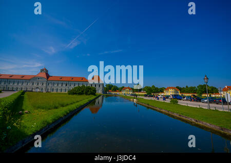 Nymphenburg, Deutschland - 30. Juli 2015: Idyllische Teil des Schlossparks mit ruhigen blauen Fluss Kanal und große Gebäude im Hintergrund. Stockfoto