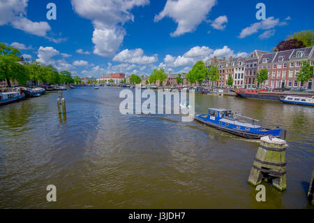 Amsterdam, Niederlande - 10. Juli 2015: Großer Wasserkanal durchzogen Stadt mit mehreren Booten geparkt neben grünen Bäumen Umgebung und bea Stockfoto