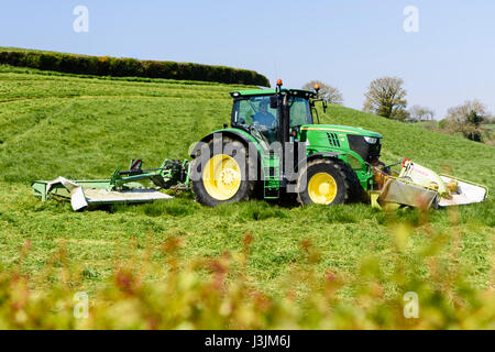 Landwirt in einen John Deere 6190 mit vorderen und hinteren Scheibenfräser Rasen schneidet die erste Ernte von Silage. Stockfoto