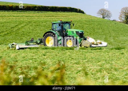 Landwirt in einen John Deere 6190 mit vorderen und hinteren Scheibenfräser Rasen schneidet die erste Ernte von Silage. Stockfoto