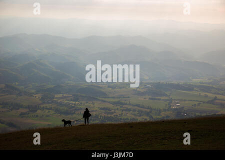 Eine Silhouette einer Frau und ein Hund auf einem Berg mit einem ein schönes Tal mit fernen Berge vor ihnen Stockfoto