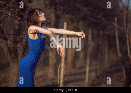 Schönes Mädchen im blauen Abendkleid steht und schaut über den Zaun. Stockfoto