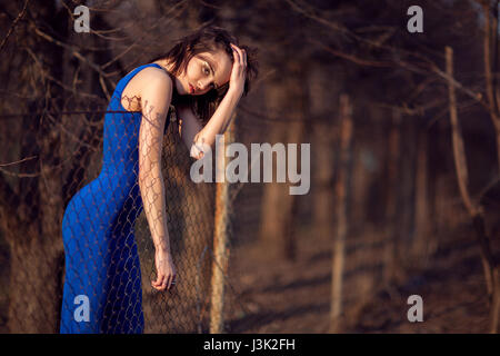 Schönes Mädchen im blauen Abendkleid steht und schaut über den Zaun. Stockfoto