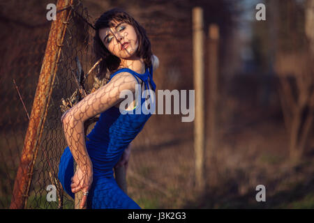 Schönes Mädchen im blauen Abendkleid Rücken gegen den Zaun gedrückt. Stockfoto
