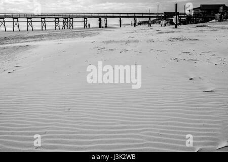 Wellen im Strandsand mit pier Stockfoto