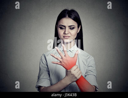 Frau hält ihr schmerzhafte Handgelenk auf graue Wand Hintergrund isoliert rot gefärbt. Stockfoto