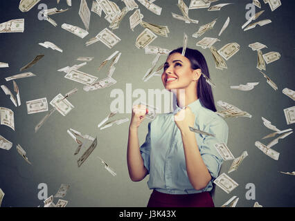 Porträt glücklich Frau frohlockt Pumpen Fäuste ekstatischen feiert Erfolg unter einem Geld Rechnungen Regen herunterfallen-Dollar-Banknoten auf grau isoliert Wand bac Stockfoto