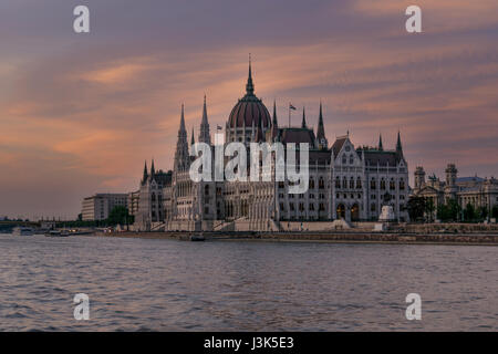 Blick auf das ungarische Parlamentsgebäude mit einem dramatischen Himmel bei Sonnenuntergang von der Donau. Stockfoto