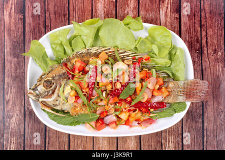 Thai-Küche, würzig und säuerlich Kräutersalat gebratene Tilapia mit Baby Tamarinde Blätter auf Holz serviert. Stockfoto