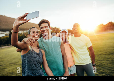 Junge sportliche Frau, die eine Selfie mit Freunden im Park. Gruppe von Jugendlichen Selbstbildnis mit Handy im Freien. Stockfoto