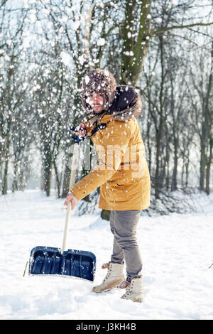 junger Mann Schneeschaufeln in der Nähe von einem kleinen Wäldchen Stockfoto