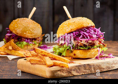 Zwei Sandwiches mit gezogenes Schweinefleisch, Pommes Frites und Glas Bier auf hölzernen Hintergrund Stockfoto