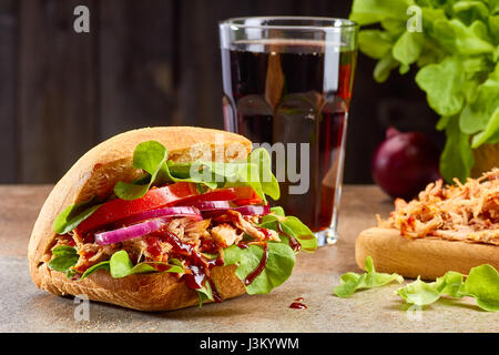 Sandwich mit zog Schweinefleisch und Glas Cola am Steintisch Stockfoto