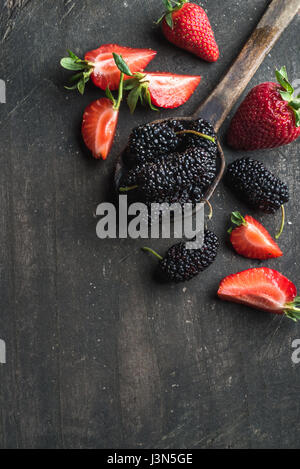 Beeren auf dunklem Holz. Frische Erdbeeren und Maulbeeren in rustikalen Kochlöffel Stockfoto