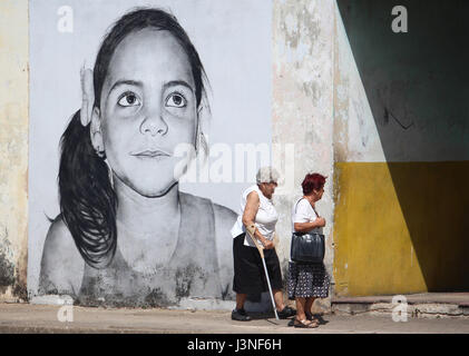 Havanna, Kuba. 24. April 2017. Zwei Frauen gehen vorbei an einem großen Bild zeigt das Gesicht eines Kindes, das auf eine Wand in Havanna, Kuba, 24. April 2017 gemalt worden ist. Streetart-Künstler Maisel Lopez zieht große Gesichter der Kinder an heruntergekommenen Wänden. Mit "Los Colosos" hofft der kubanischen Maler, Kunst auf die Straße zu bringen. Foto: Guillermo Nova/Dpa/Alamy Live News Stockfoto