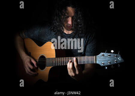 Junger Mann mit lockigem Haar eine akustische Gitarre zu spielen. Stockfoto