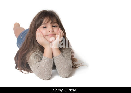 Lächelndes cooles Brünette langhaarige Mädchen liegt auf der hellgrauen Hintergrund. Das Mädchen unterstützt ihr Kinn mit beiden Händen. Stockfoto
