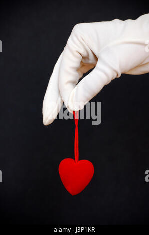 Hand im weißen Handschuh hält eine rotes Herz-Form über einen schwarzen Hintergrund, Liebe Konzept Stockfoto