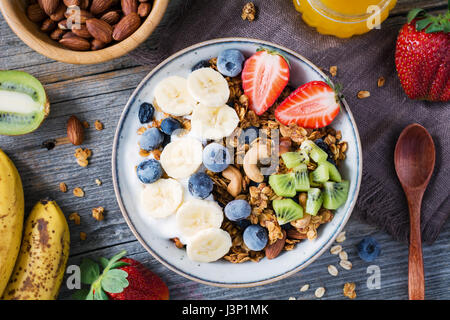 Hausgemachtem Müsli mit Nüssen und Rosinen, Kiwi, Heidelbeeren, Bananen, Erdbeeren und Joghurt. Ansicht von oben. Konzept der gesunden Lebensweise Stockfoto