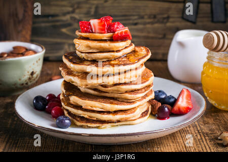 Gesunden Pfannkuchen. Stapel von köstliche gesunde Vollkorn-Pfannkuchen mit Dinkelmehl, serviert mit Erdbeeren, Blaubeeren, Preiselbeeren, Mandeln, Honig Stockfoto