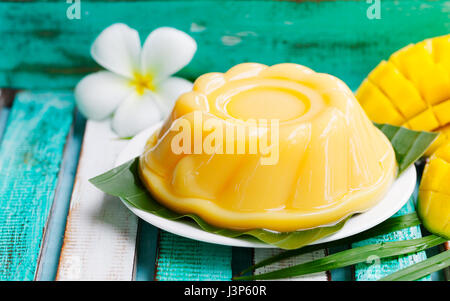 Mango-Pudding, Gelee auf weißen Teller mit Palmzweig. Bunten hölzernen Hintergrund. Stockfoto