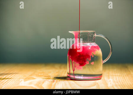 Roter Farbe fallen in einen Glaskrug mit Wasser gefüllt. Stockfoto