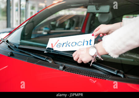 Junge Frau steckt ein Schild mit dem Text Verkocht unter die Scheibenwischer eines verkauften Autos in einer garage Stockfoto