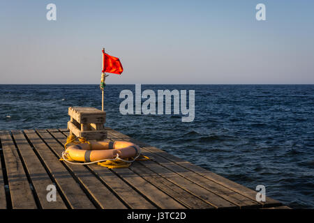 Rote Fahne für Warnung und Rettungsring auf einem alten hölzernen Pier zum Tauchen und Schnorcheln am sunset.copy Platz. Stockfoto