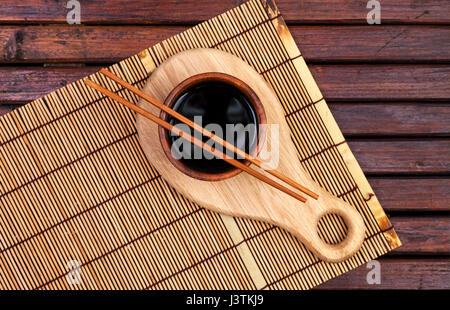 Bambus Matte, Sojasauce, Stäbchen auf dunklen Holztisch. Draufsicht mit Textfreiraum Stockfoto