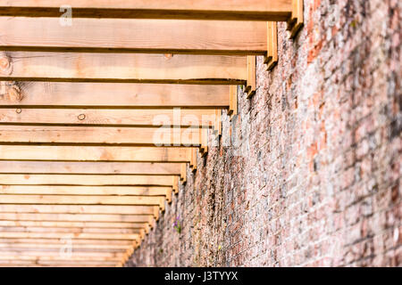 Schweren Holzbalken einer neu errichteten Pergola an der Mauer von einem ummauerten Garten angeschlossen. Stockfoto