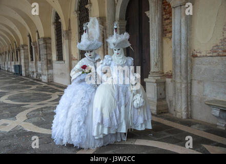 Bild von zwei Personen in komplementären kunstvollen Kostümen entlang des Dogenpalastes während des Karnevalfestes in Venedig, Italien. Stockfoto