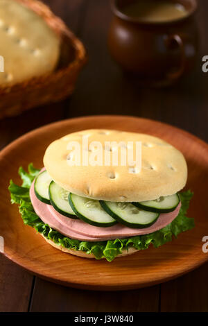 Traditionellen chilenischen Hallulla Brötchen zubereitet als Sandwich mit Salat, Aufschnitt und Gurken serviert auf Holzplatte Stockfoto