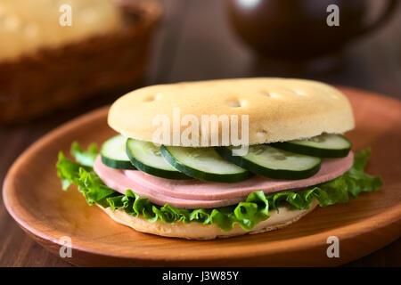Traditionellen chilenischen Hallulla Brötchen zubereitet als Sandwich mit Salat, Aufschnitt und Gurken serviert auf Holzplatte Stockfoto