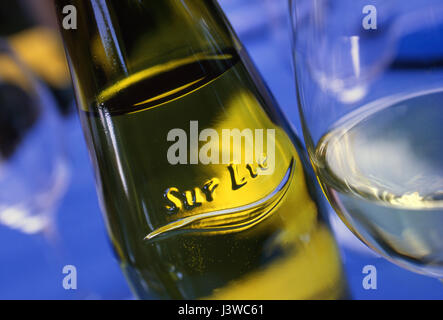 Blick auf Muscadet Sur Lie auf Weinflasche mit Reliefetikett, das „Sur Lie“ bezeichnet, und gegossenes Glas trockenen französischen Weißweins auf einem blauen Alfresco-Tisch Stockfoto