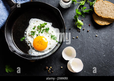 Spiegelei. Nahaufnahme der das Spiegelei auf einer Pfanne. Gesalzene und gewürzte Spiegelei mit Petersilie auf gusseisernen Pfanne und schwarzen Hintergrund. Stockfoto