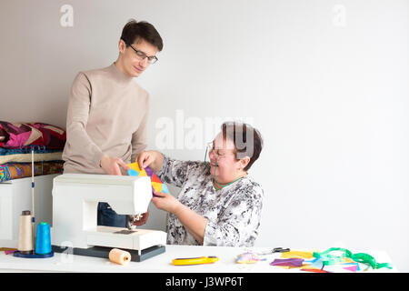 Patchwork und Quilting - zwei lächelnde Schneider bei der Arbeit im Studio mit bunten Patchwork Tuch liegen auf dem Tisch neben der Nähmaschine neben den Faden, Schere, Nadeln, Maßband. Stockfoto