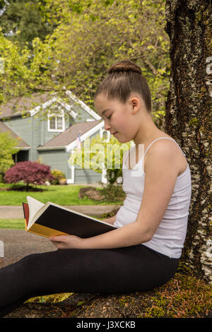 Elf Jahre altes Mädchen ein Buch im Schatten eines Baumes in Issaquah, Washington, USA Stockfoto