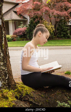 Elf Jahre altes Mädchen ein Buch im Schatten eines Baumes in Issaquah, Washington, USA Stockfoto