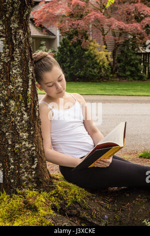 Elf Jahre altes Mädchen ein Buch im Schatten eines Baumes in Issaquah, Washington, USA Stockfoto