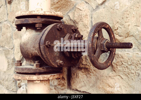 Alten Wasserventil auf einem Hintergrund von einer Natursteinmauer. Große und rostige Ventil an der Wasserleitung Nahaufnahme Stockfoto