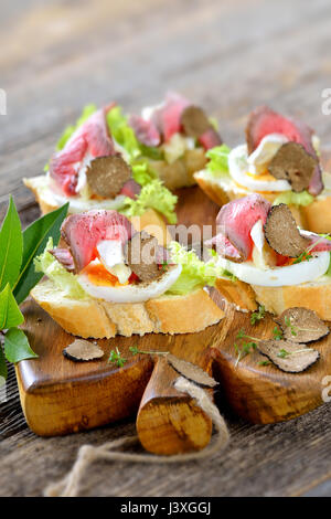 Canapes mit Roastbeef, schwarze Herbst Trüffel, französischer Brie Käse auf eine Scheibe Ei auf Baguette mit einem Blatt Salat Stockfoto