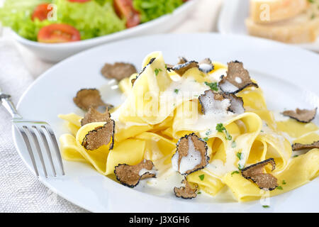 Italienische Papardelle mit frischen schwarzen Herbst Trüffel und Sahnesoße, im Hintergrund einen gemischten Salat und Scheiben baguette Stockfoto