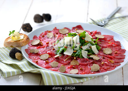 Köstliches Rindfleisch-Carpaccio mit in Scheiben geschnittenen schwarzen Trüffeln, Rucola-Salat mit Parmesan und gerösteten Pinienkernen, serviert mit einer Scheibe geröstetes baguette Stockfoto